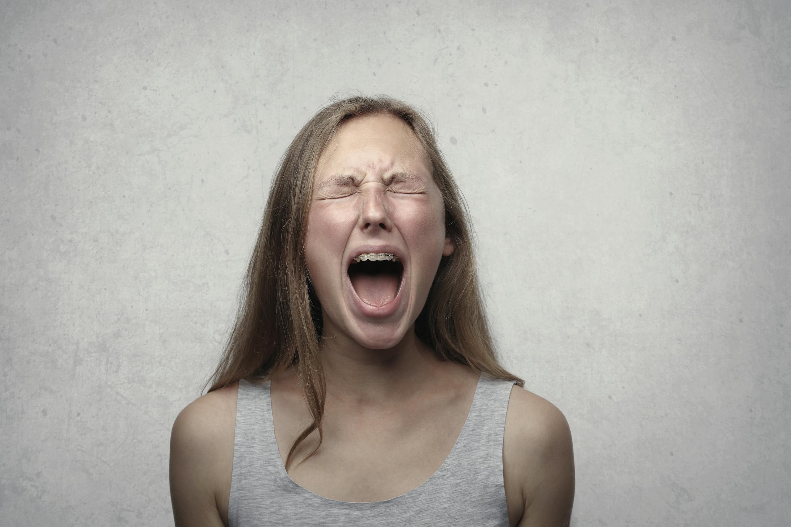Young woman screaming with emotion showing braces against gray backdrop.
