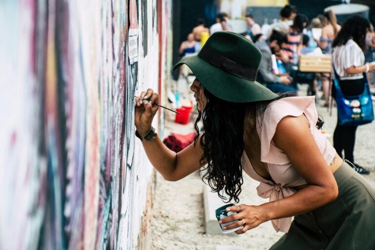 Young woman wearing hat painting mural on urban street wall during daytime