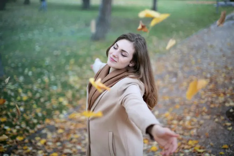 Young woman with outstretched arms delighting in fallen autumn leaves in Paris park