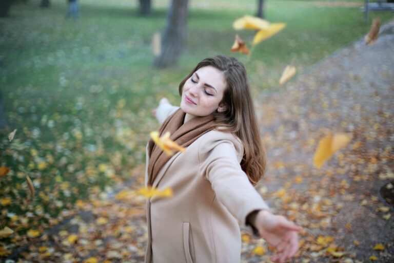 Young woman with outstretched arms delighting in fallen autumn leaves in Paris park