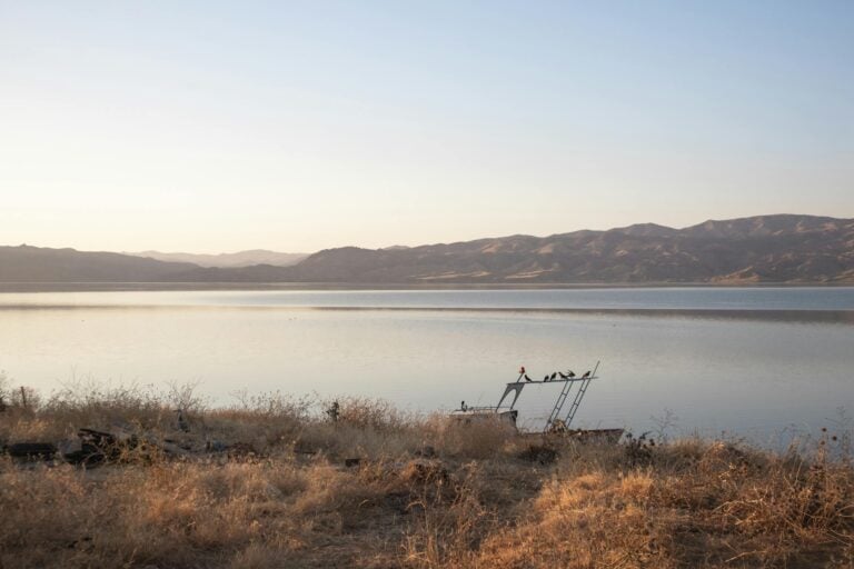 Solitary boat on calm lake with dry grass shore and distant mountains