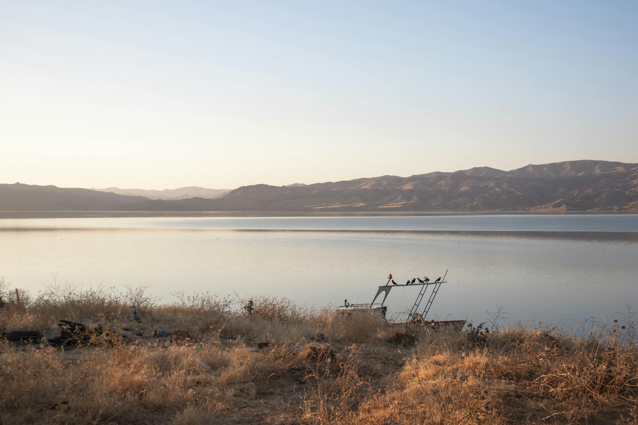 Solitary boat on calm lake with dry grass shore and distant mountains