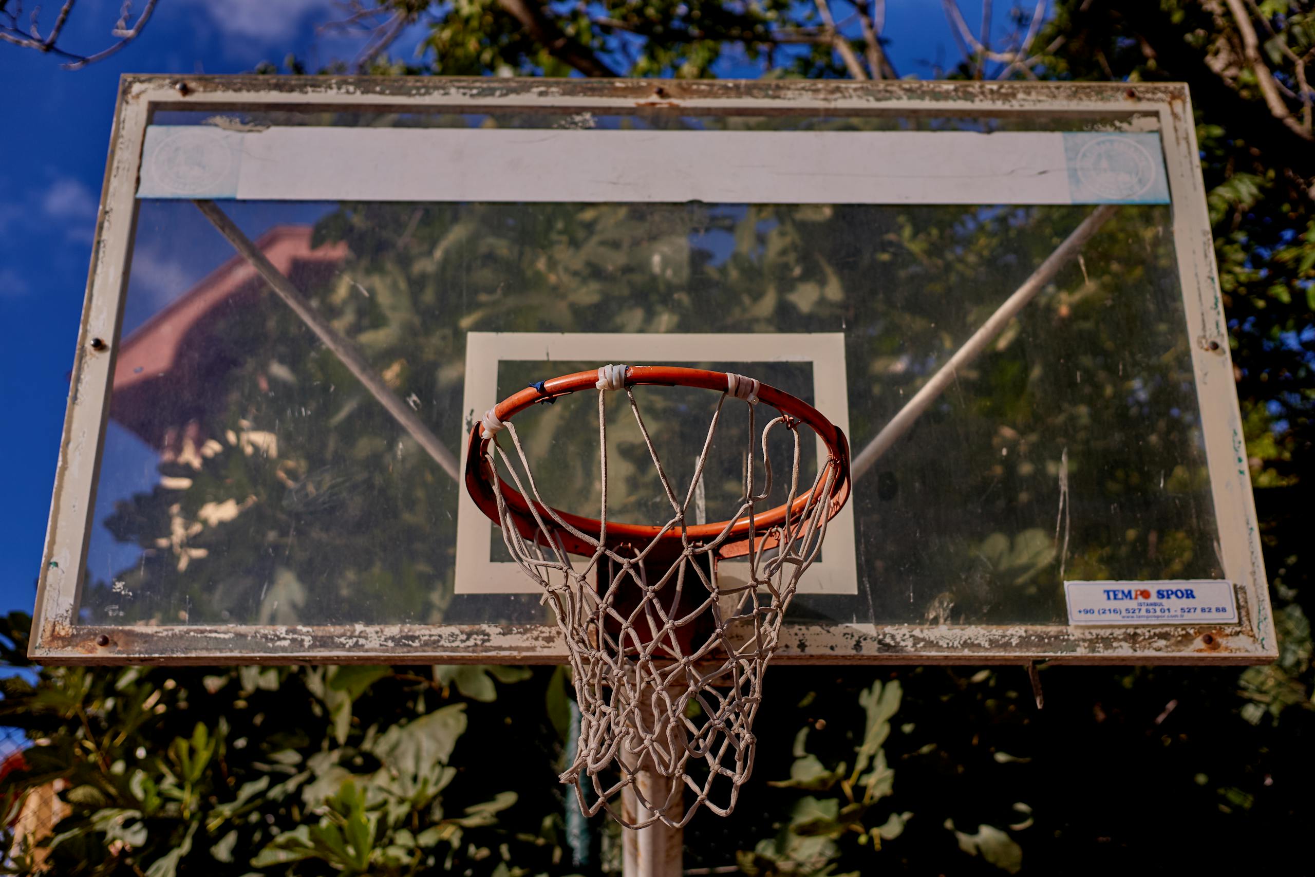 Weathered outdoor basketball hoop with red rim against blue sky and trees