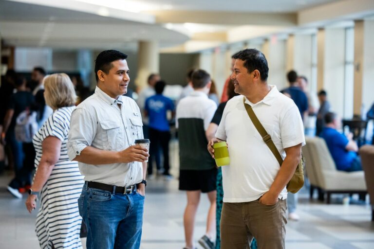 Two men engage in friendly conversation at a community event, holding beverages.