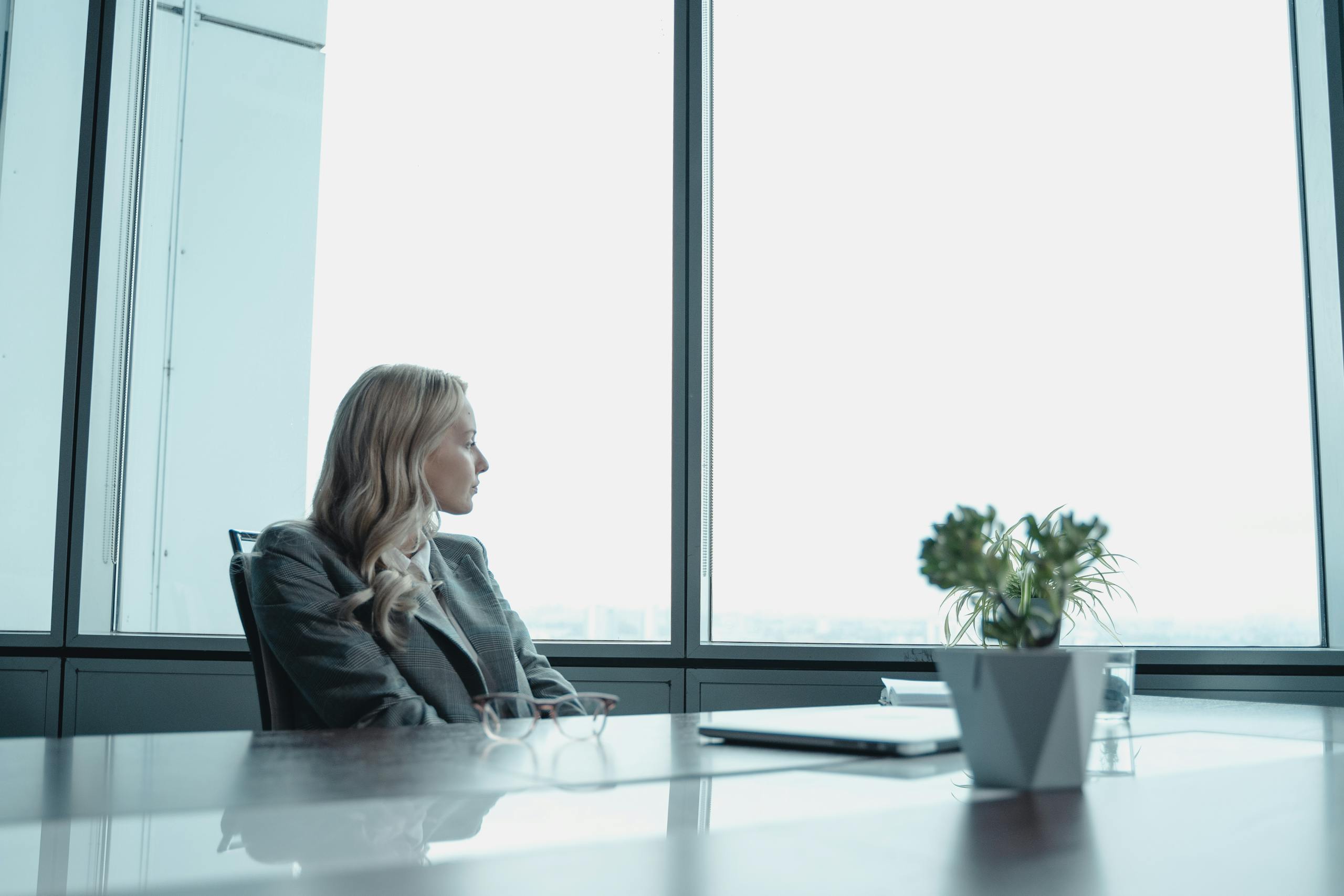Businesswoman in suit looking out window of contemporary office with modern setup.
