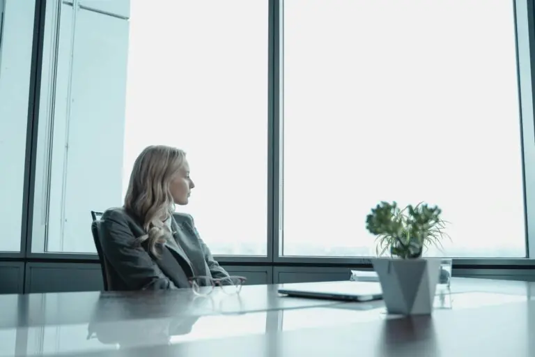 Businesswoman in suit looking out window of contemporary office with modern setup.