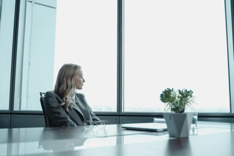 Businesswoman in suit looking out window of contemporary office with modern setup.