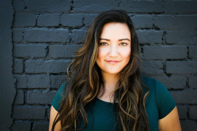 Portrait of confident woman with long brunette hair smiling in front of brick wall.