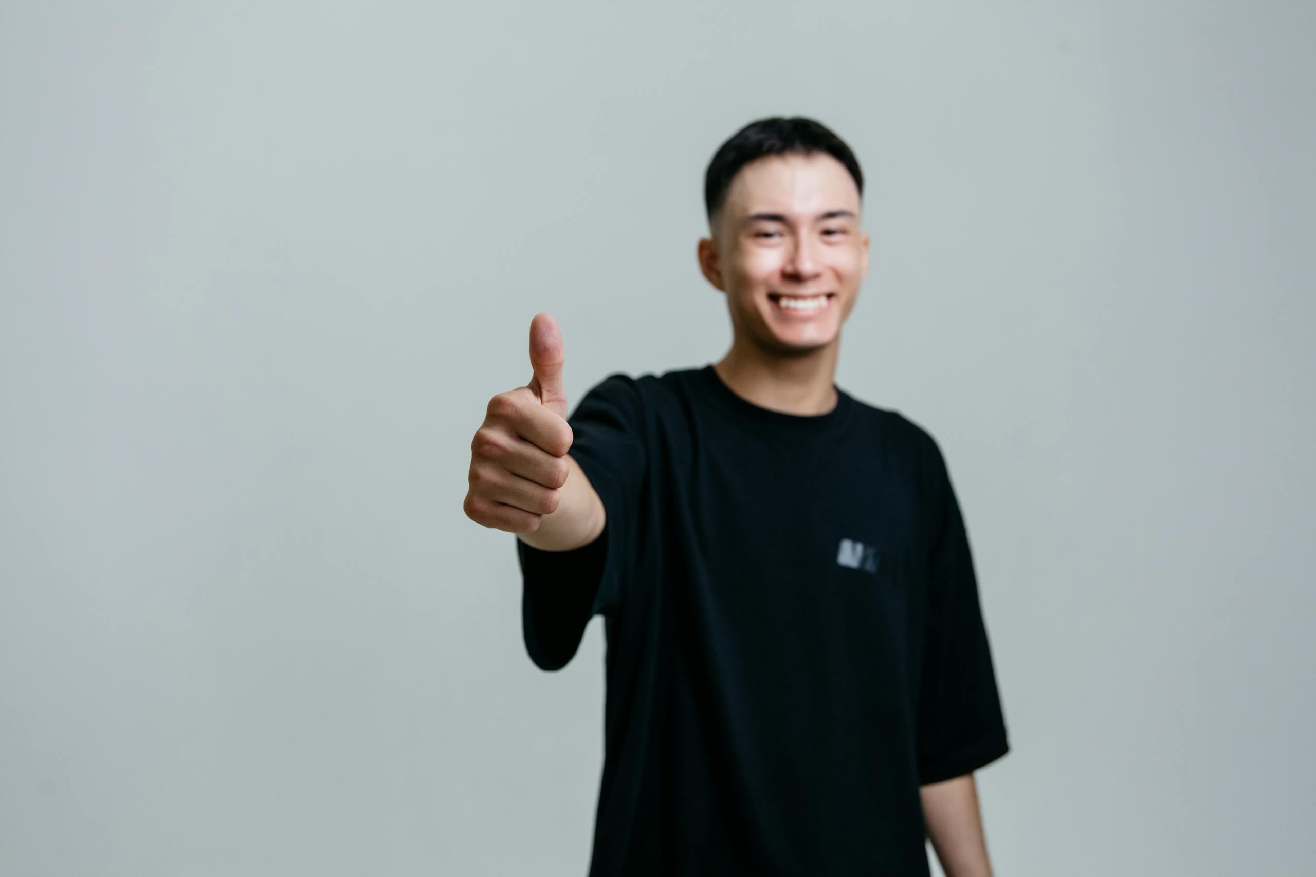 Cheerful young man in black shirt smiles and gives thumbs up studio setting