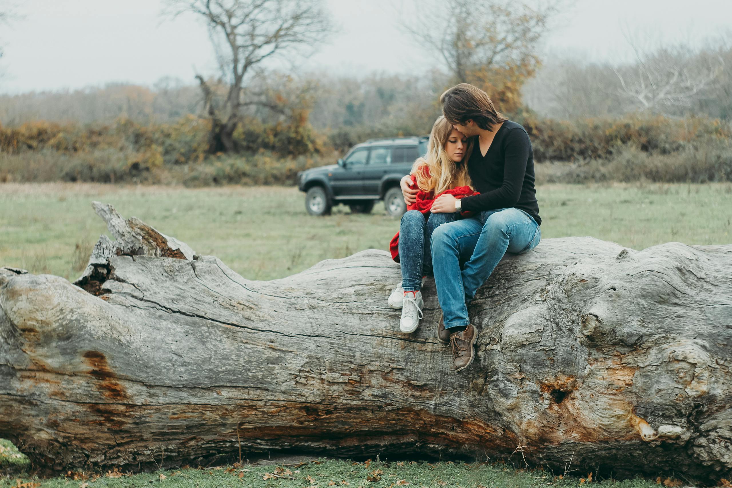 Couple embracing tenderly on large fallen tree against serene natural landscape.