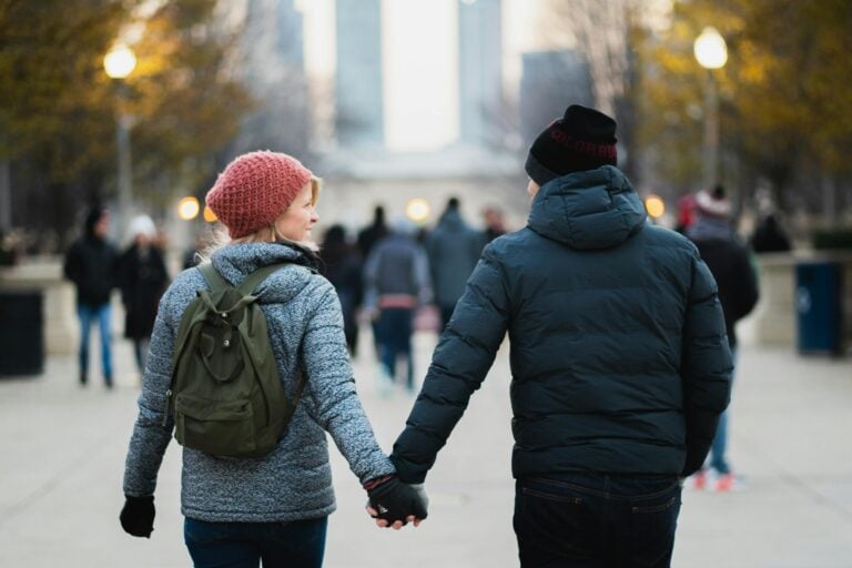 Couple holds hands on winter day in urban park capturing warmth and connection
