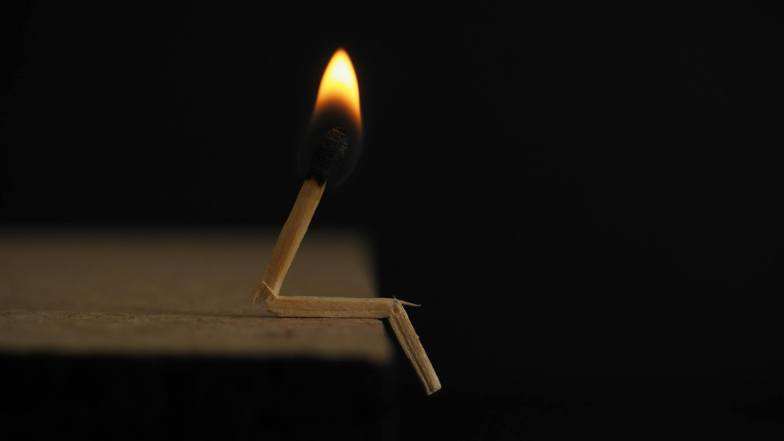 Bent burning matchstick with flame against dark background symbolizing struggle.