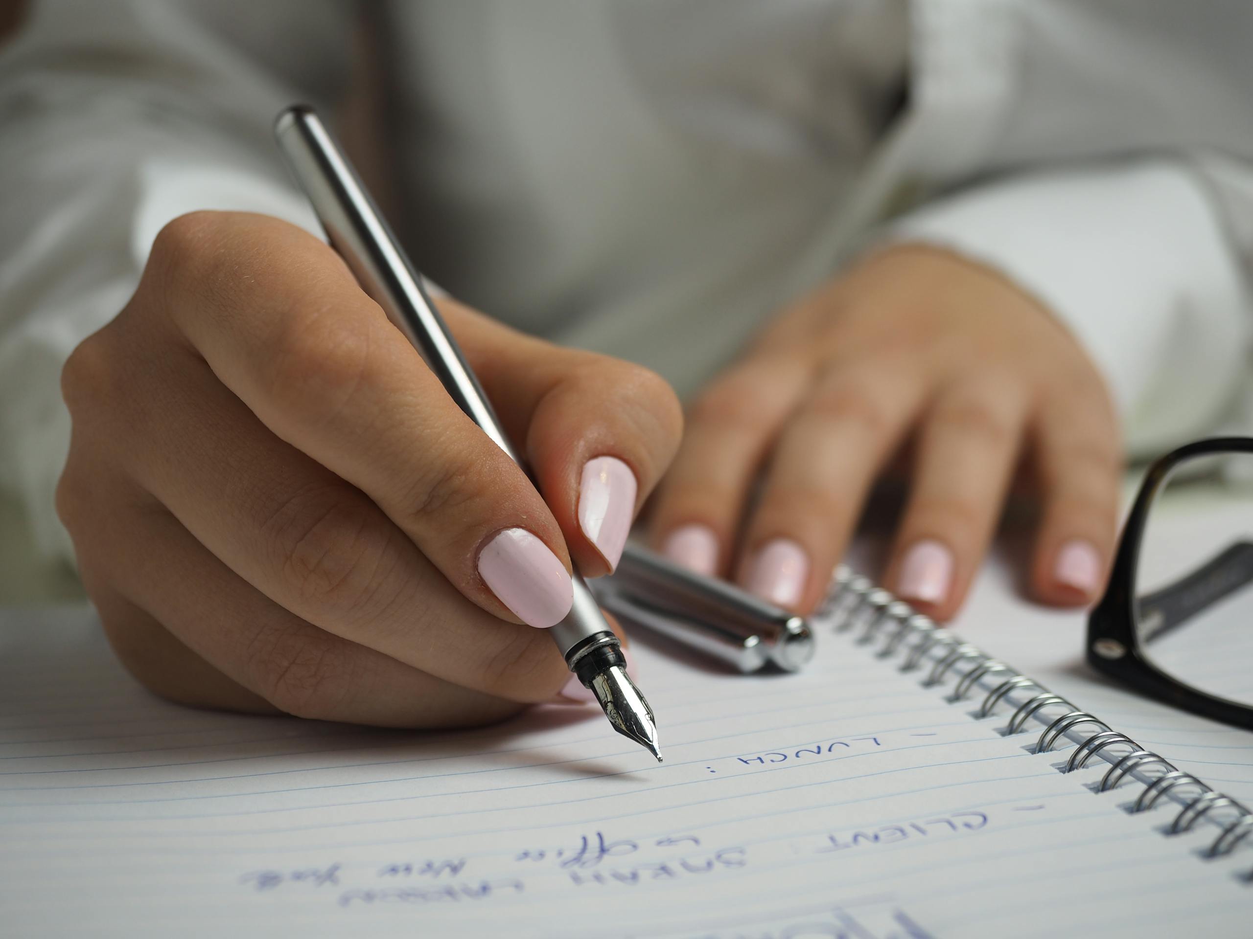 Close-up of handwriting in notebook with fountain pen and glasses