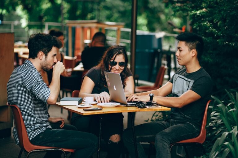 Group of young adults collaborating on laptop at outdoor coffee shop enjoying teamwork
