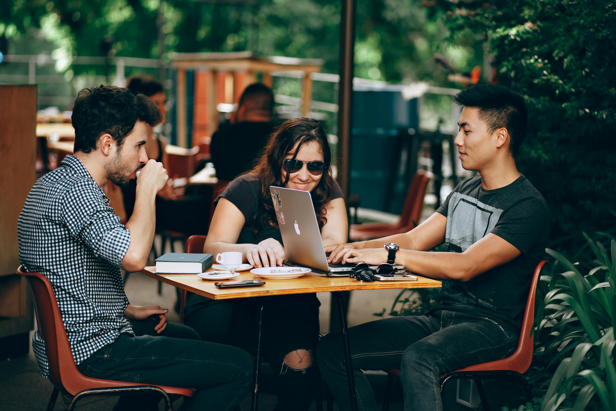 Group of young adults collaborating on laptop at outdoor coffee shop enjoying teamwork