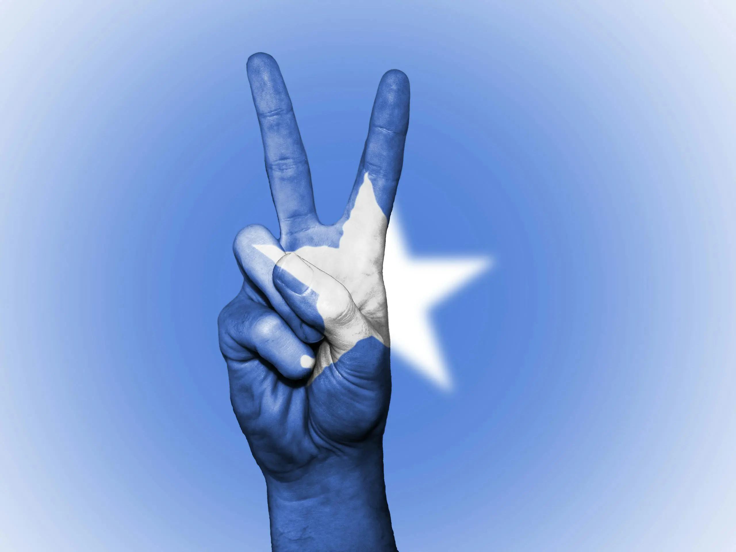 Hand making peace gesture painted with Somali flag colors symbolizing national unity.
