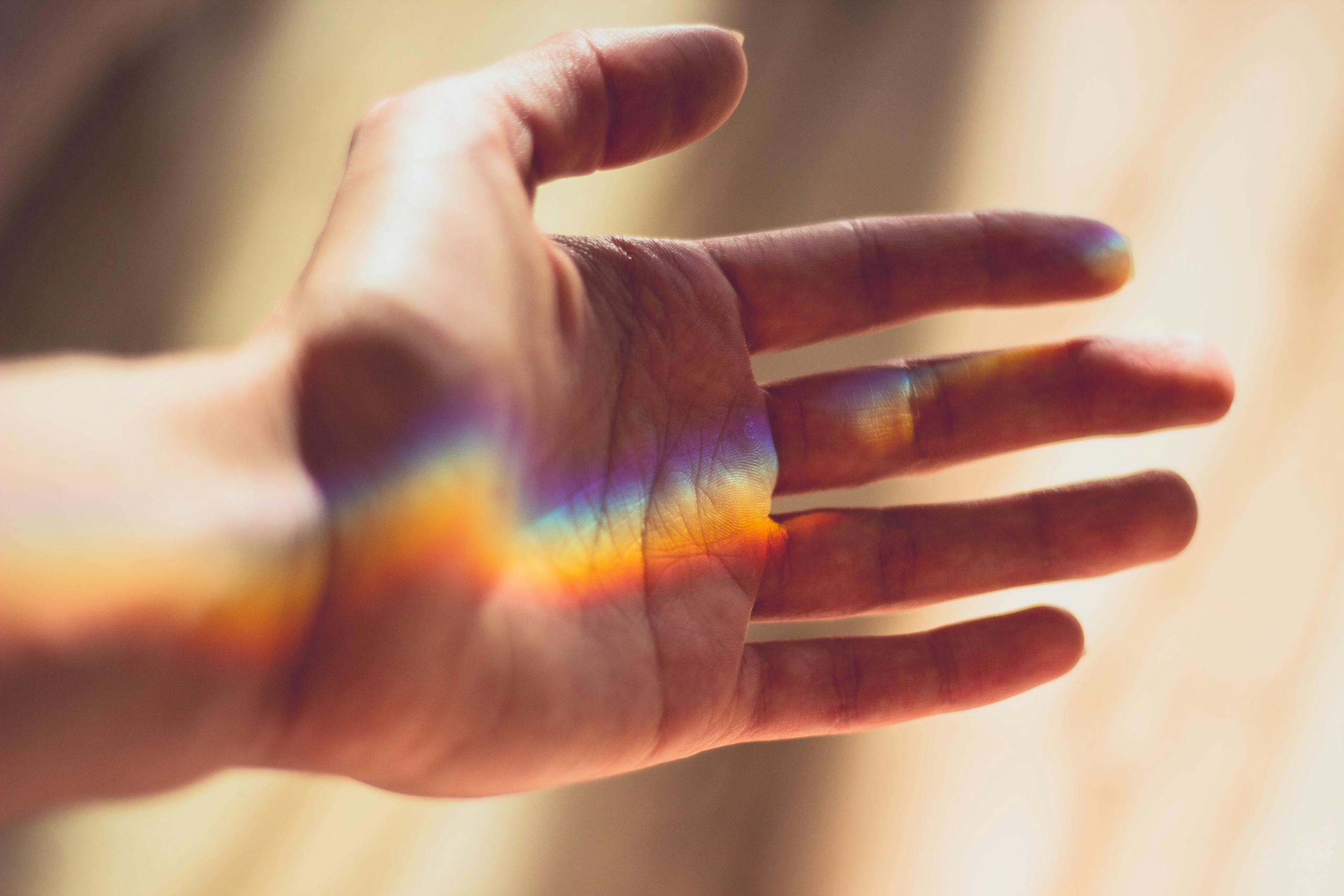 Hand displaying beautiful rainbow light refraction pattern across palm.