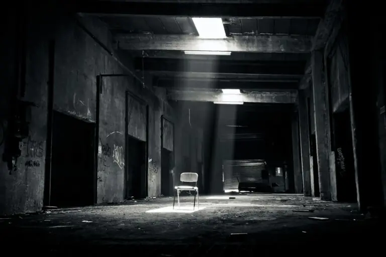 Black and white abandoned warehouse with solitary chair lit by sunlight.