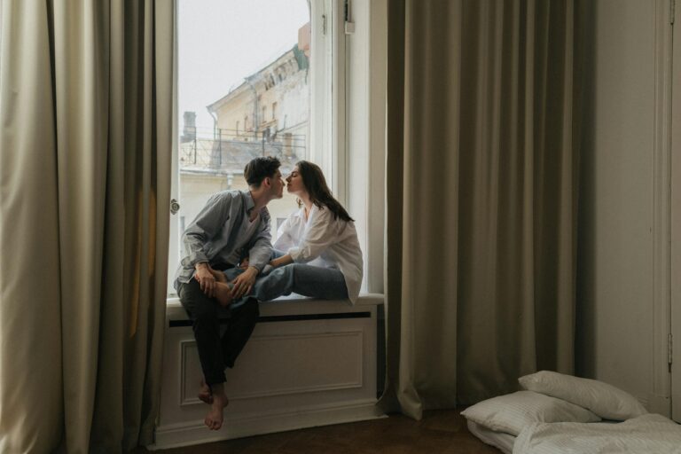 Loving couple sharing tender kiss on cozy indoor windowsill.