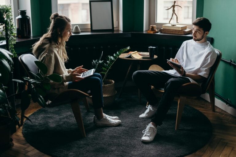 Man and woman conversing in a plant-filled minimalist home office with modern furniture.