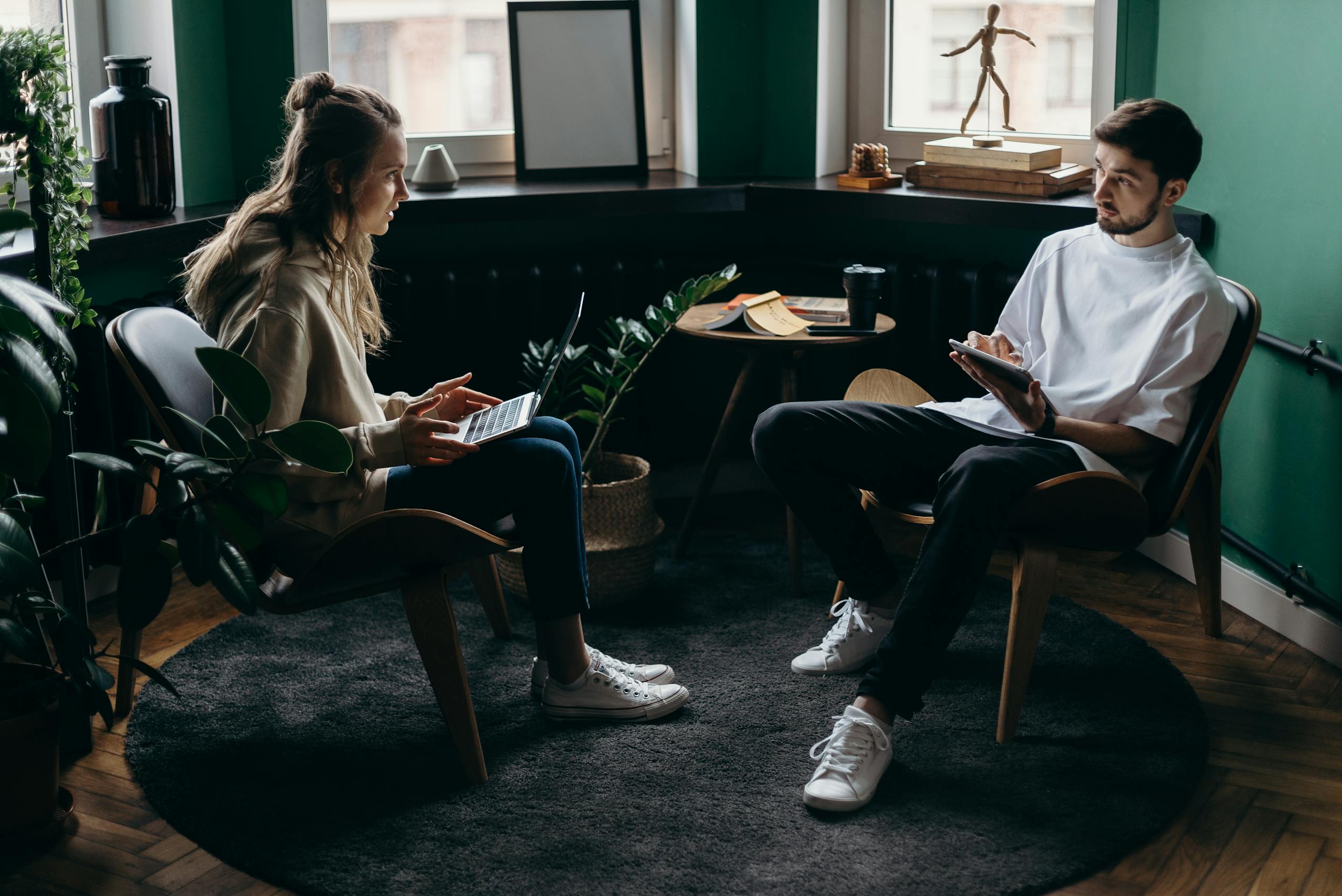 Man and woman conversing in a plant-filled minimalist home office with modern furniture.