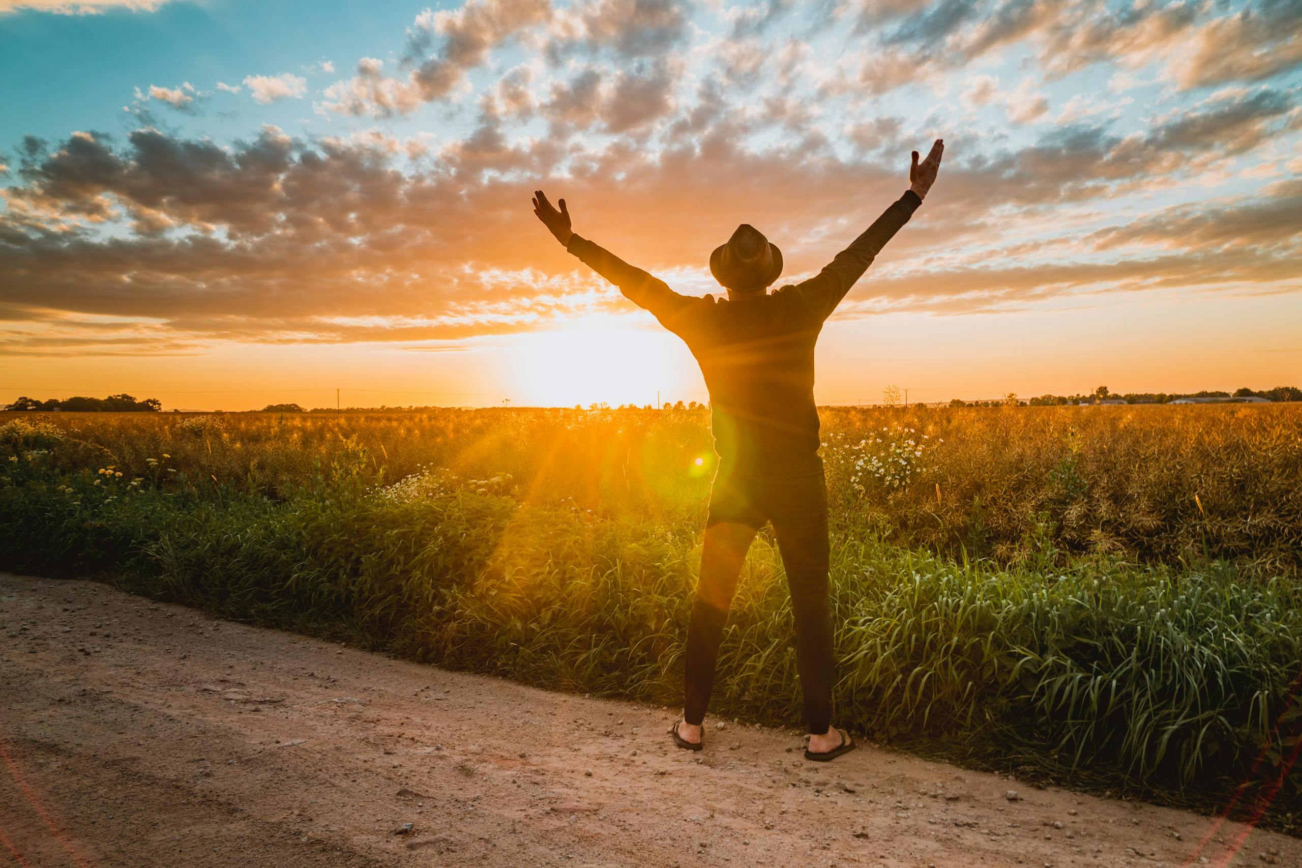 Man raising arms at sunrise in rural field expressing joy and nature connection.