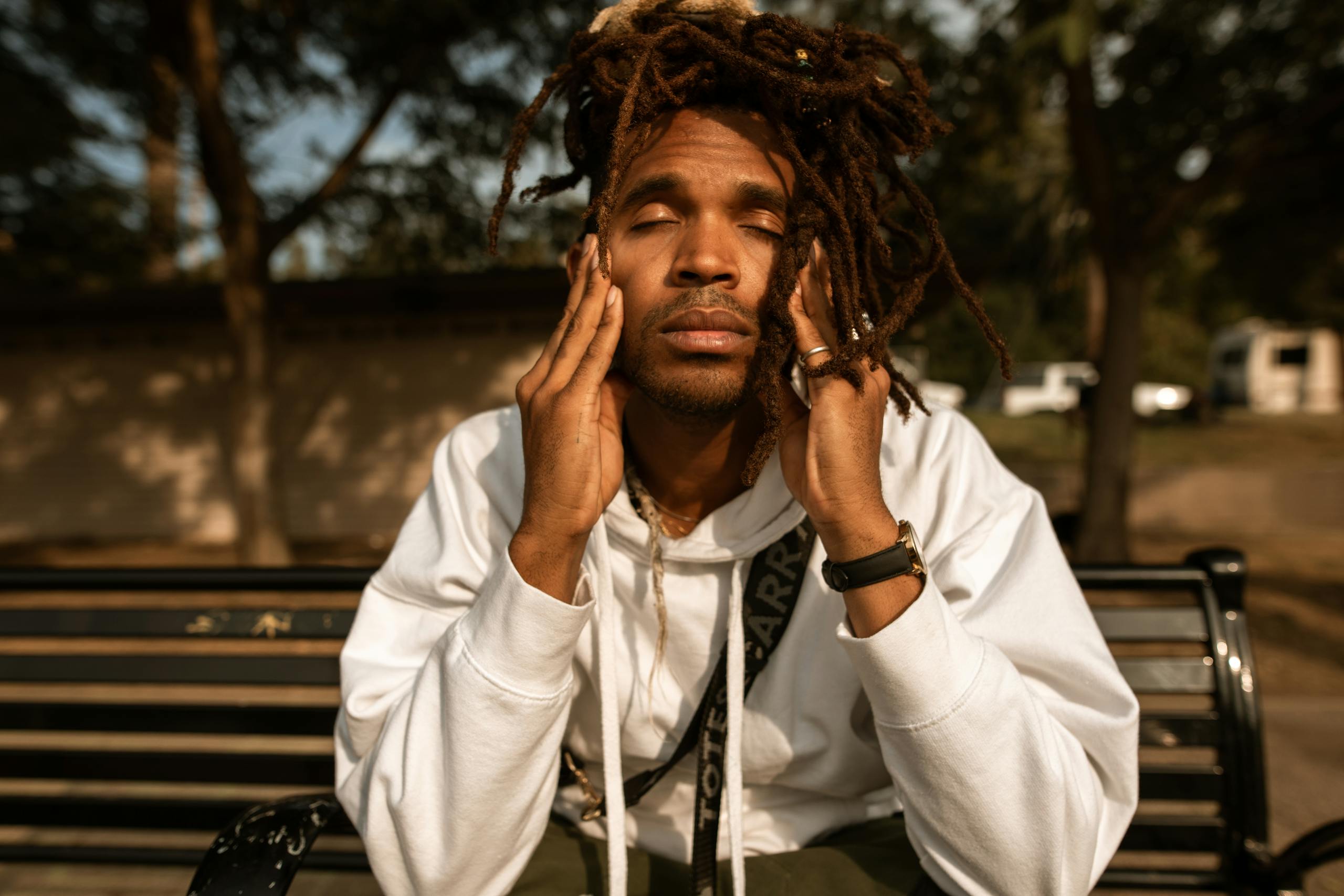 Man with dreadlocks sits on park bench contemplating with eyes closed