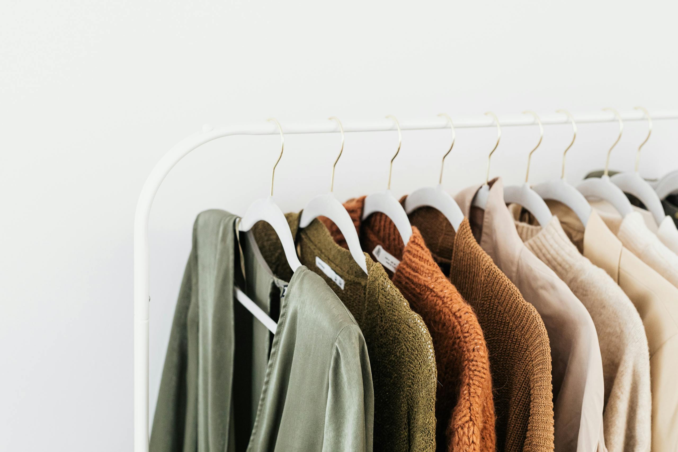 Minimalist display of colorful sweaters and shirts on white wooden hangers.