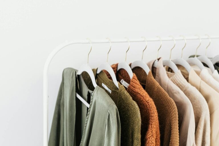 Minimalist display of colorful sweaters and shirts on white wooden hangers.