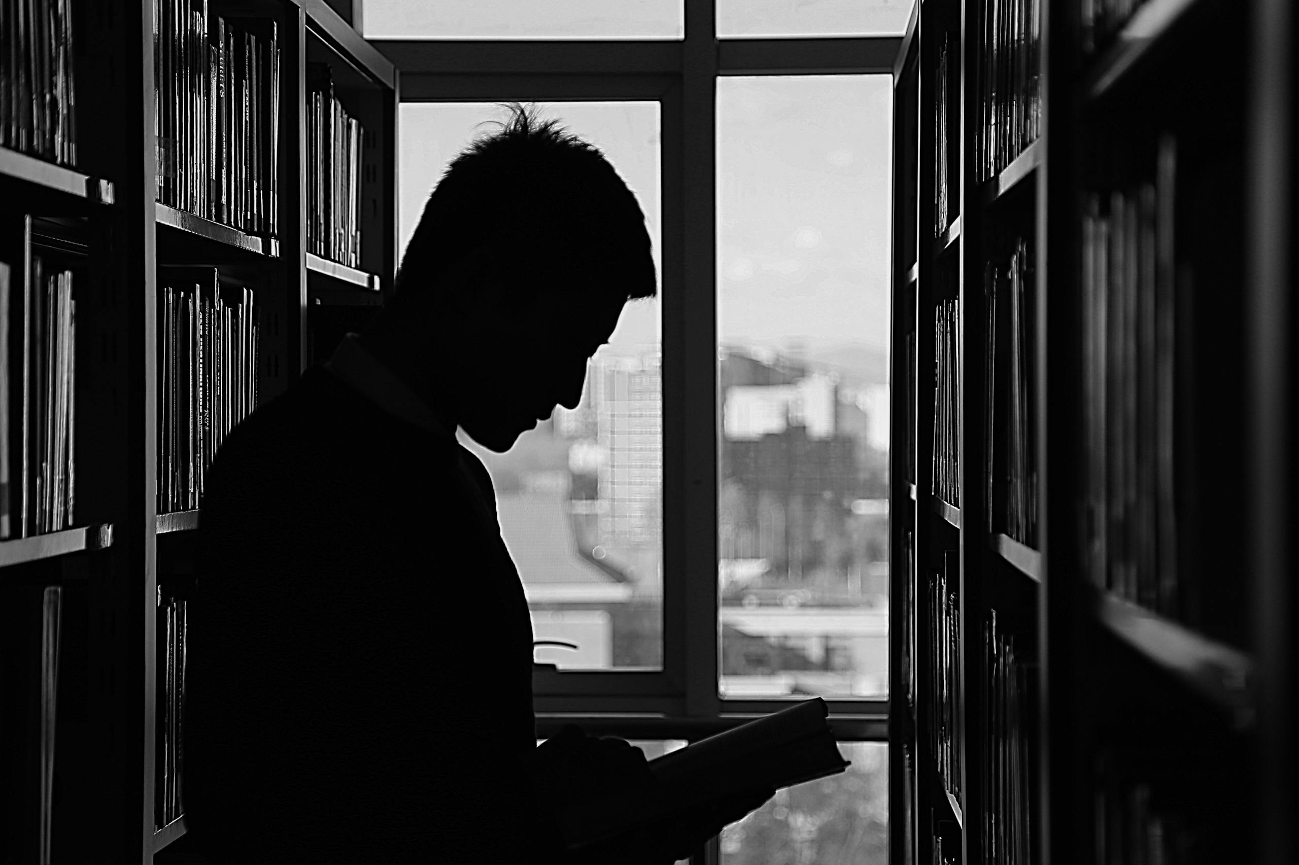 Moody silhouette of man reading in library evoking solitude and contemplation