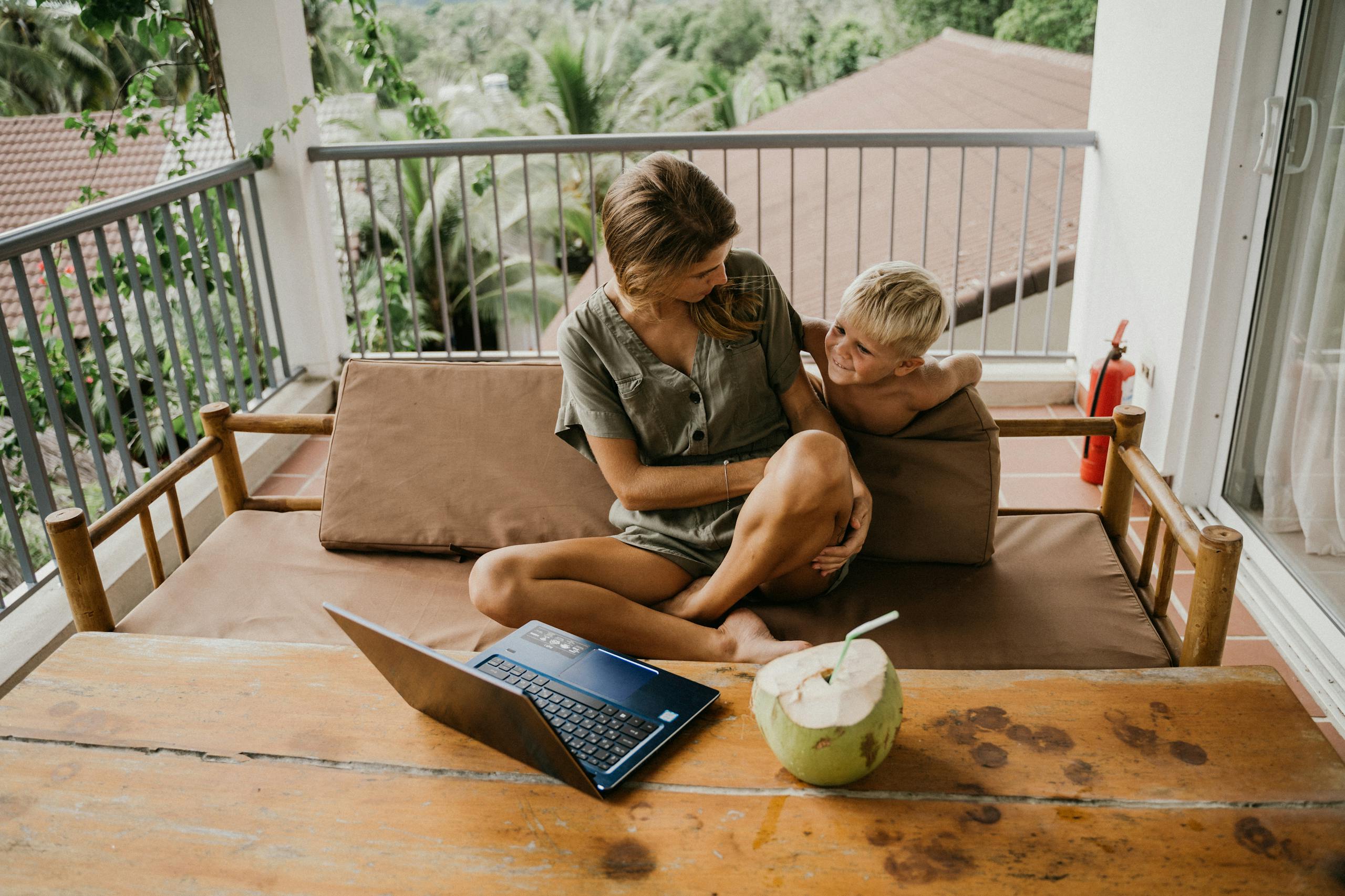 Mother and son relaxing together on balcony with laptop and coconut