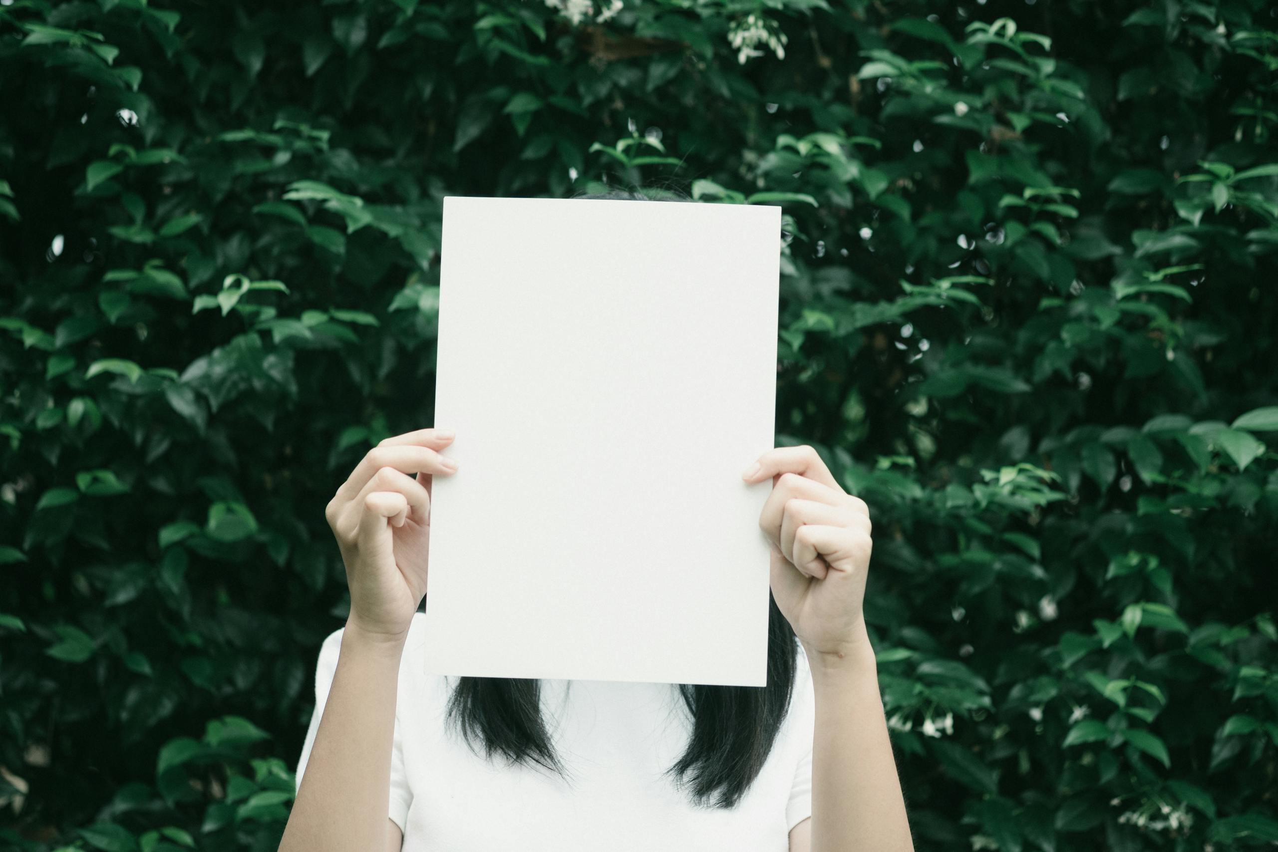 Person holding blank paper against lush leafy green background symbolically.