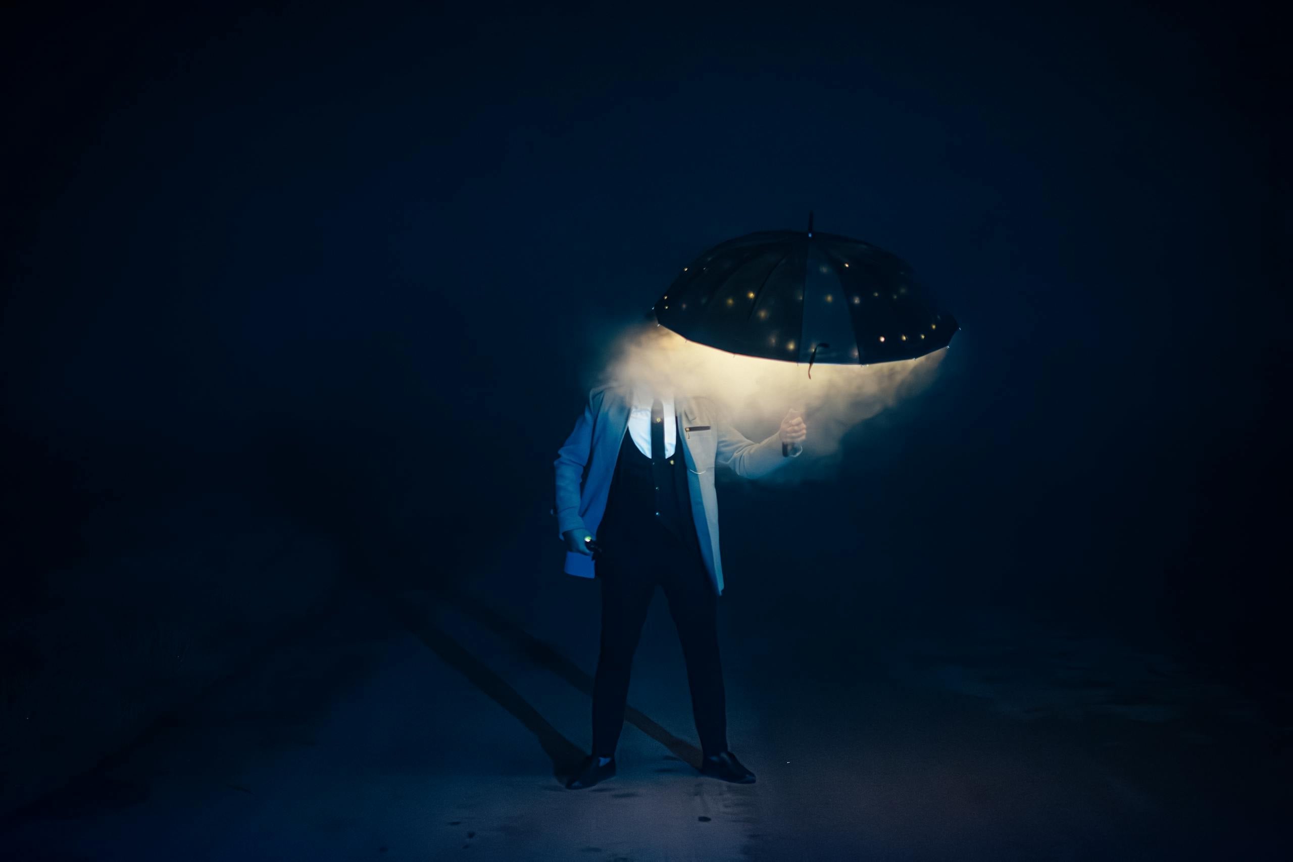 Person in suit stands in foggy darkness holding LED lit umbrella creating mysterious scene