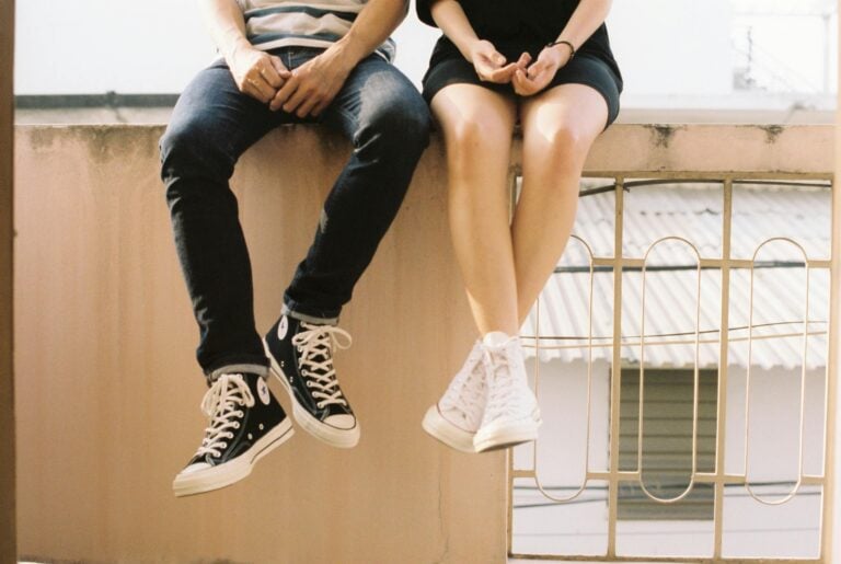 Relaxed couple sitting on ledge wearing stylish sneakers showcasing togetherness.