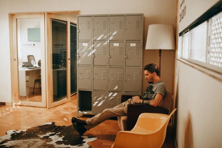 Relaxed man sits in contemporary office featuring lockers and stylish furniture creating cozy workspace