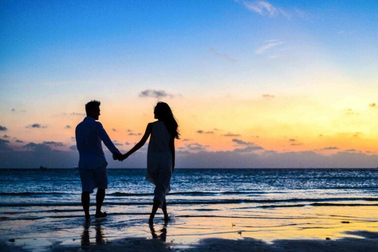 Romantic couple walks hand in hand on tropical beach at sunset enjoying serene moment