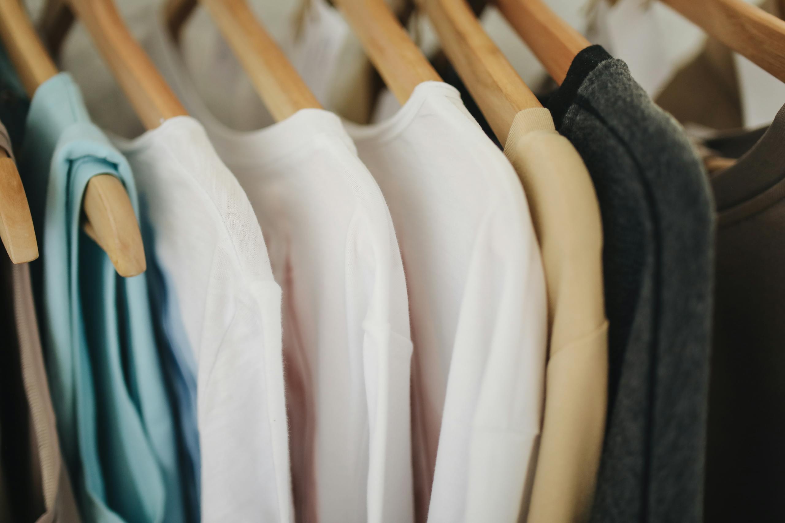 Colorful clothes neatly organized on wooden hangers in retail store display.