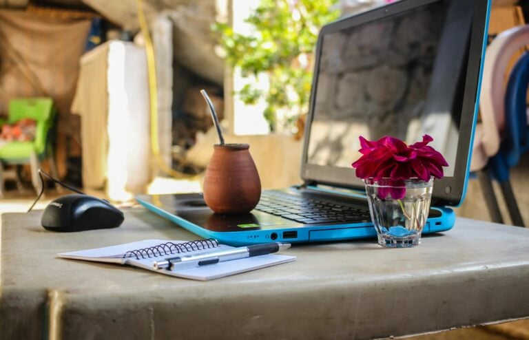 Serene outdoor workspace with laptop, notebook, mug, and fresh flowers on desk