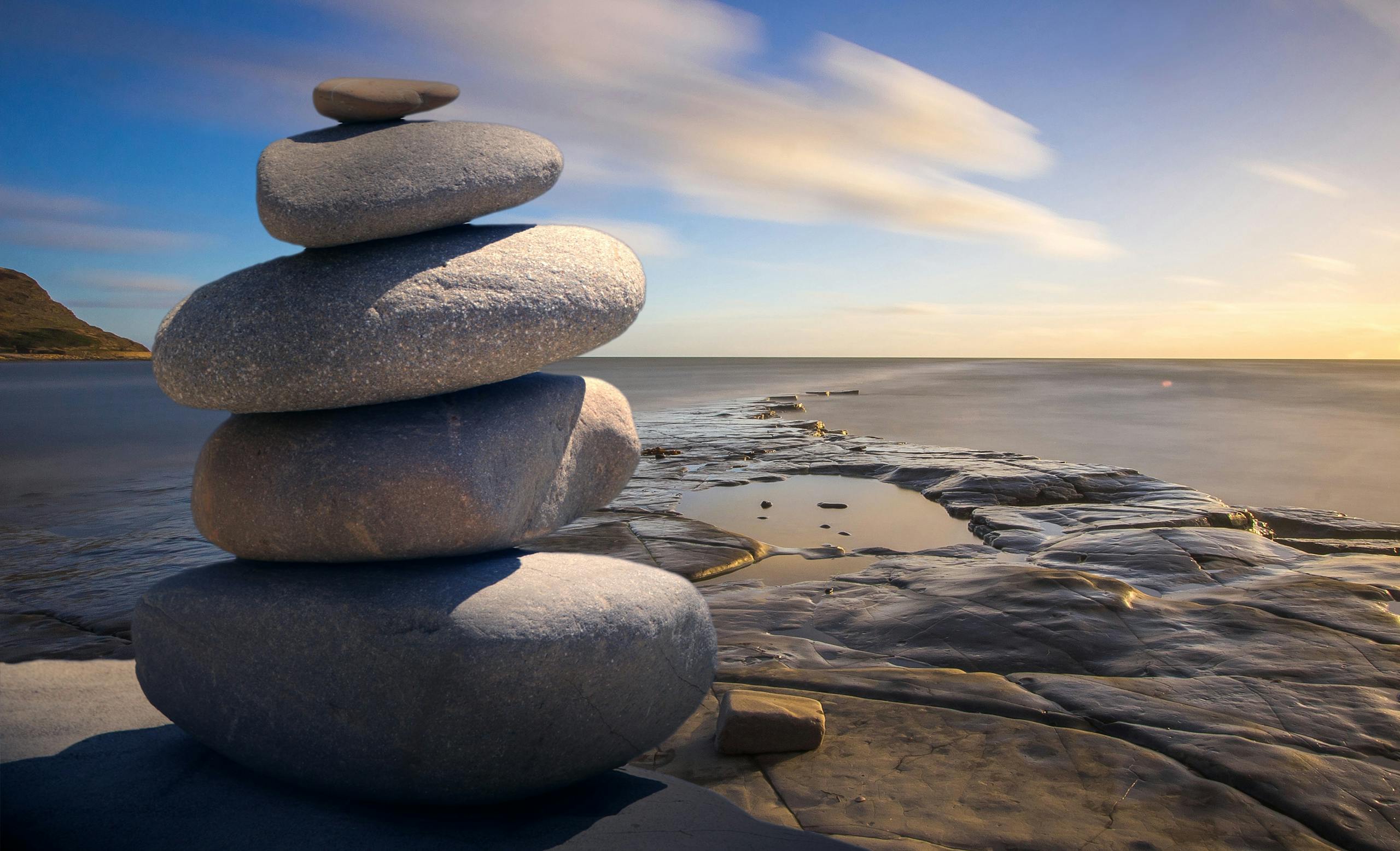 Balanced stack of stones on rocky seashore at serene sunrise.