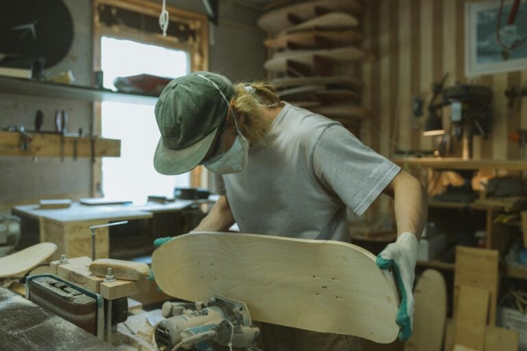 Skilled craftsman using router to shape skateboard deck in workshop setting.