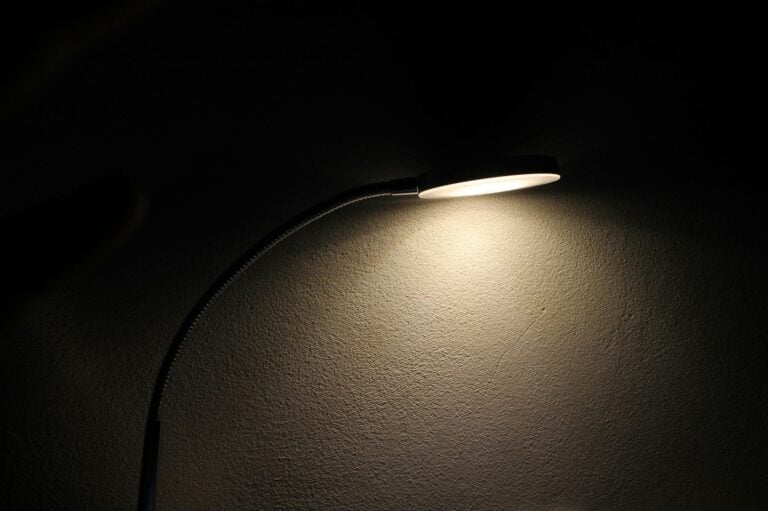 Sleek desk lamp casting soft glow on textured wall creating mood.