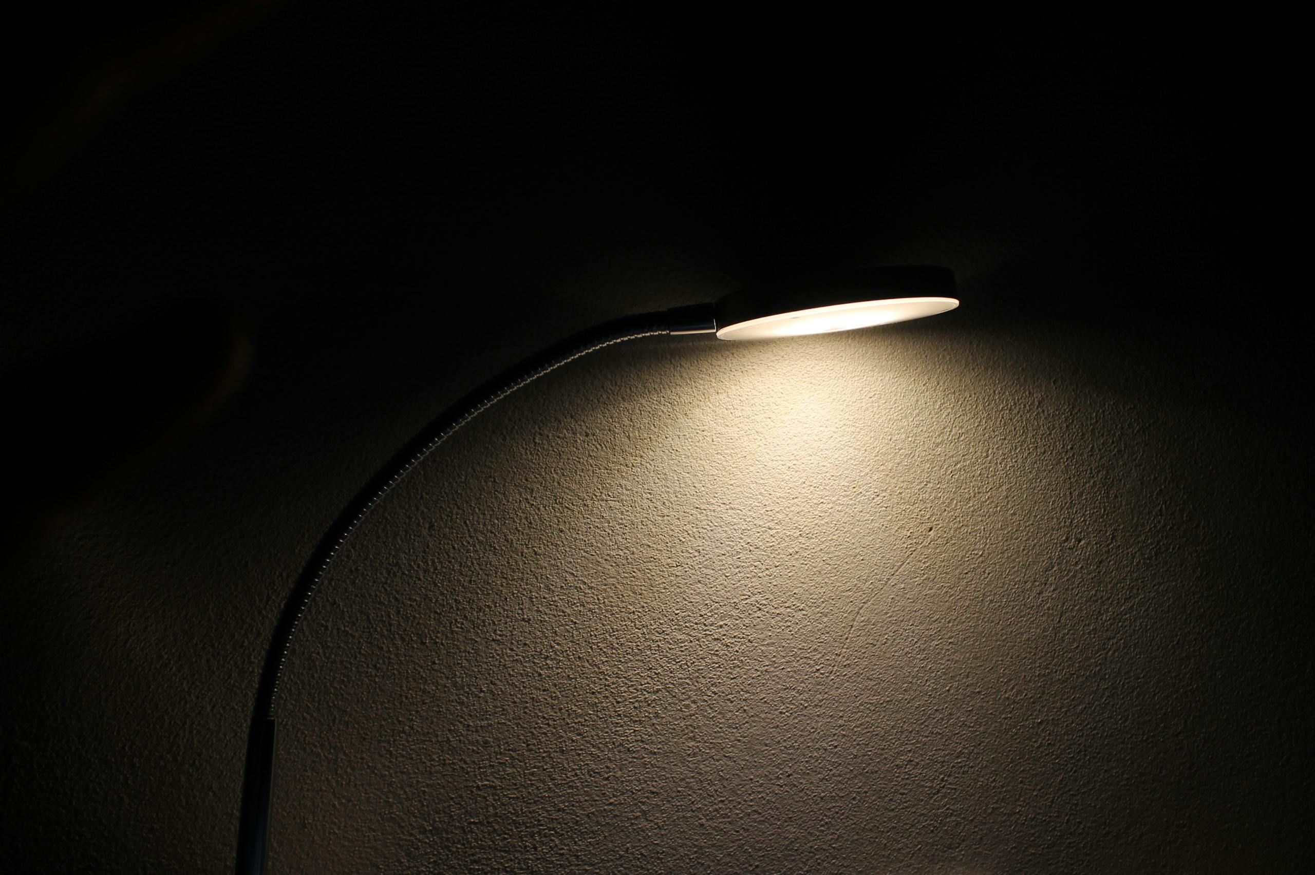 Sleek desk lamp casting soft glow on textured wall creating mood.