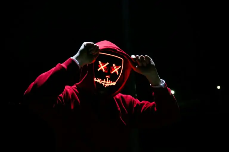 Spooky illuminated mask figure wearing red hoodie in darkness