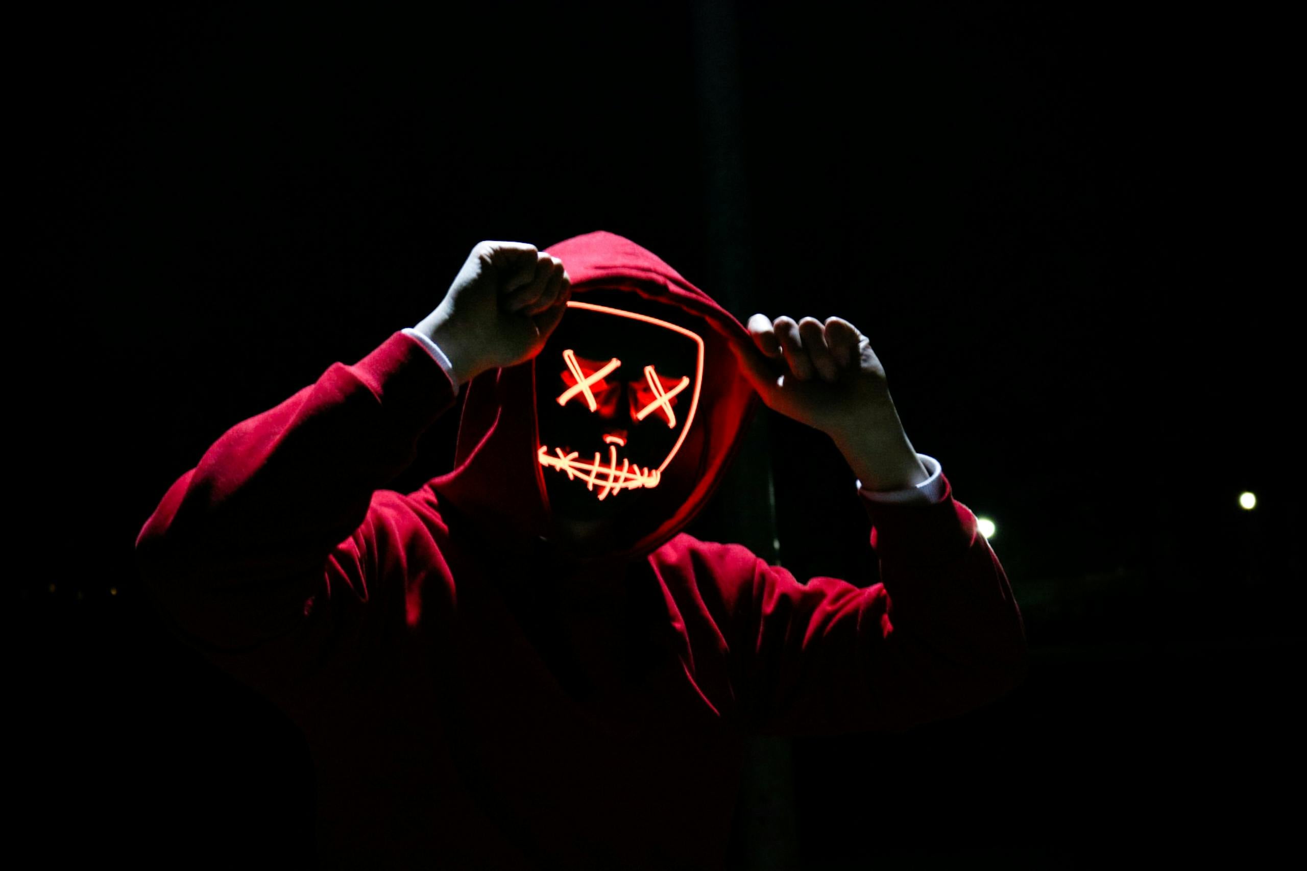 Spooky illuminated mask figure wearing red hoodie in darkness