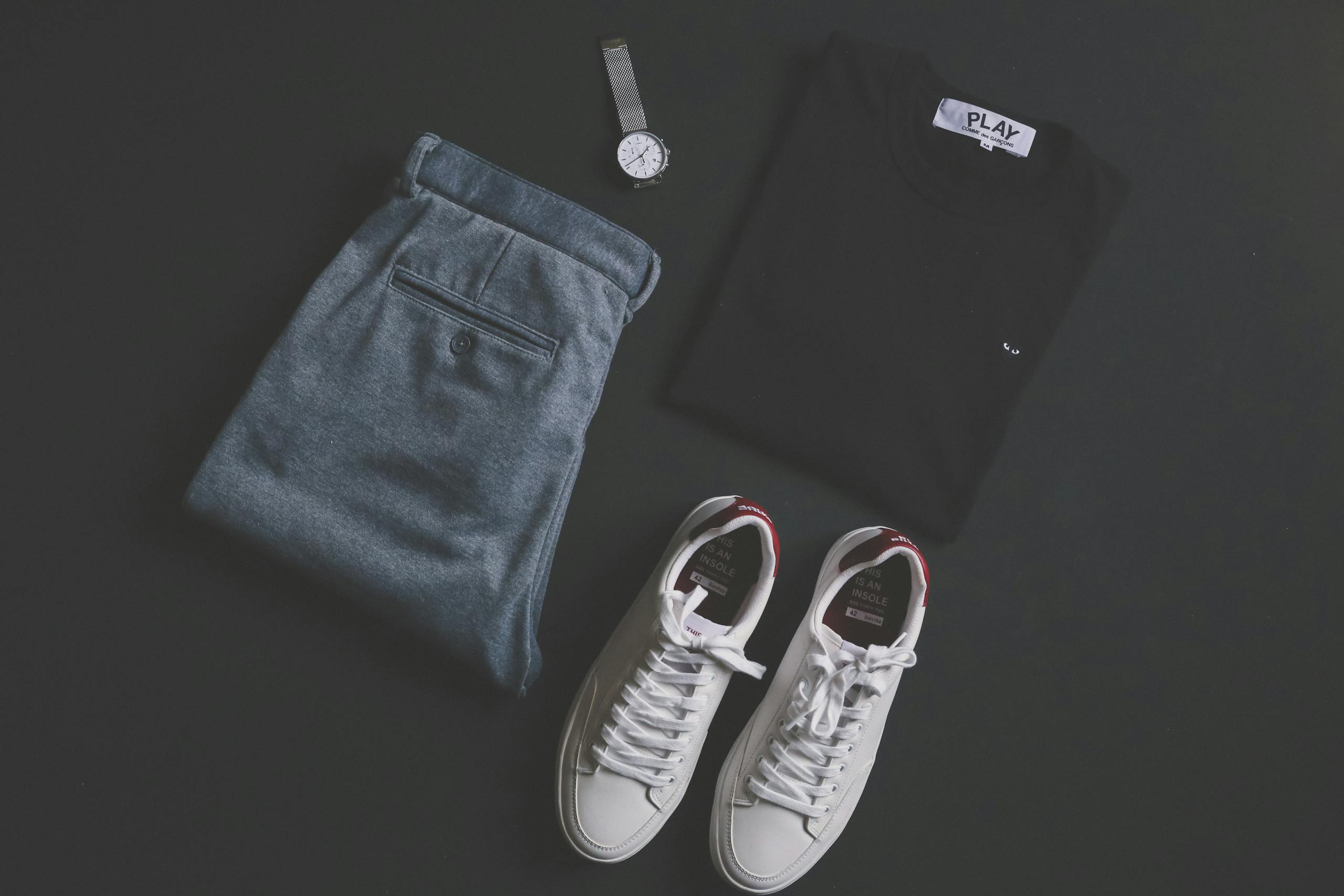 a stylish flat lay featuring jeans t shirt sneakers and a wristwatch on a dark background.