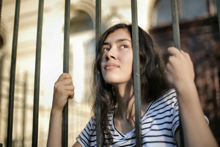 Teenage girl gazing thoughtfully through bars symbolizing hope and freedom