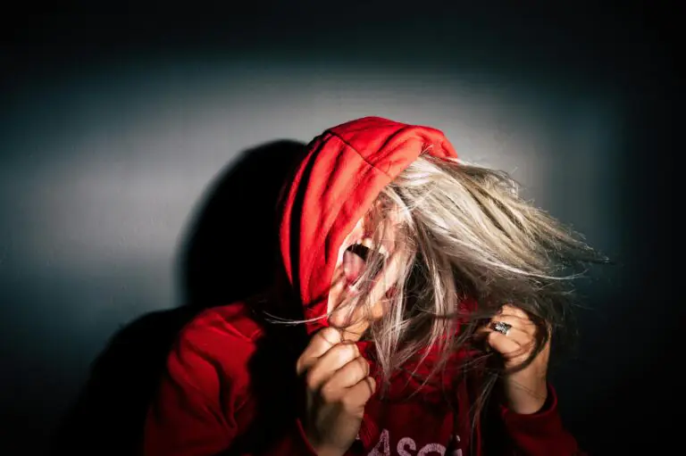 Teenager in red hoodie screams with hair flying conveying intense emotion.