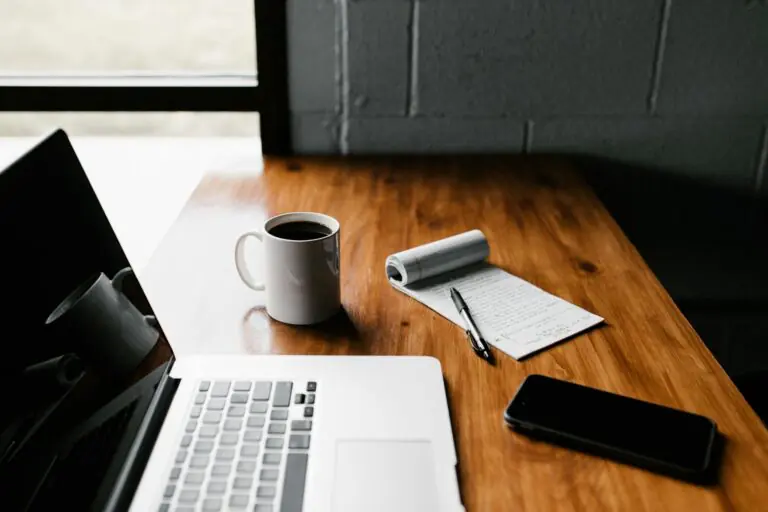 Tidy workspace featuring laptop, coffee cup, phone, notepad on wooden desk.
