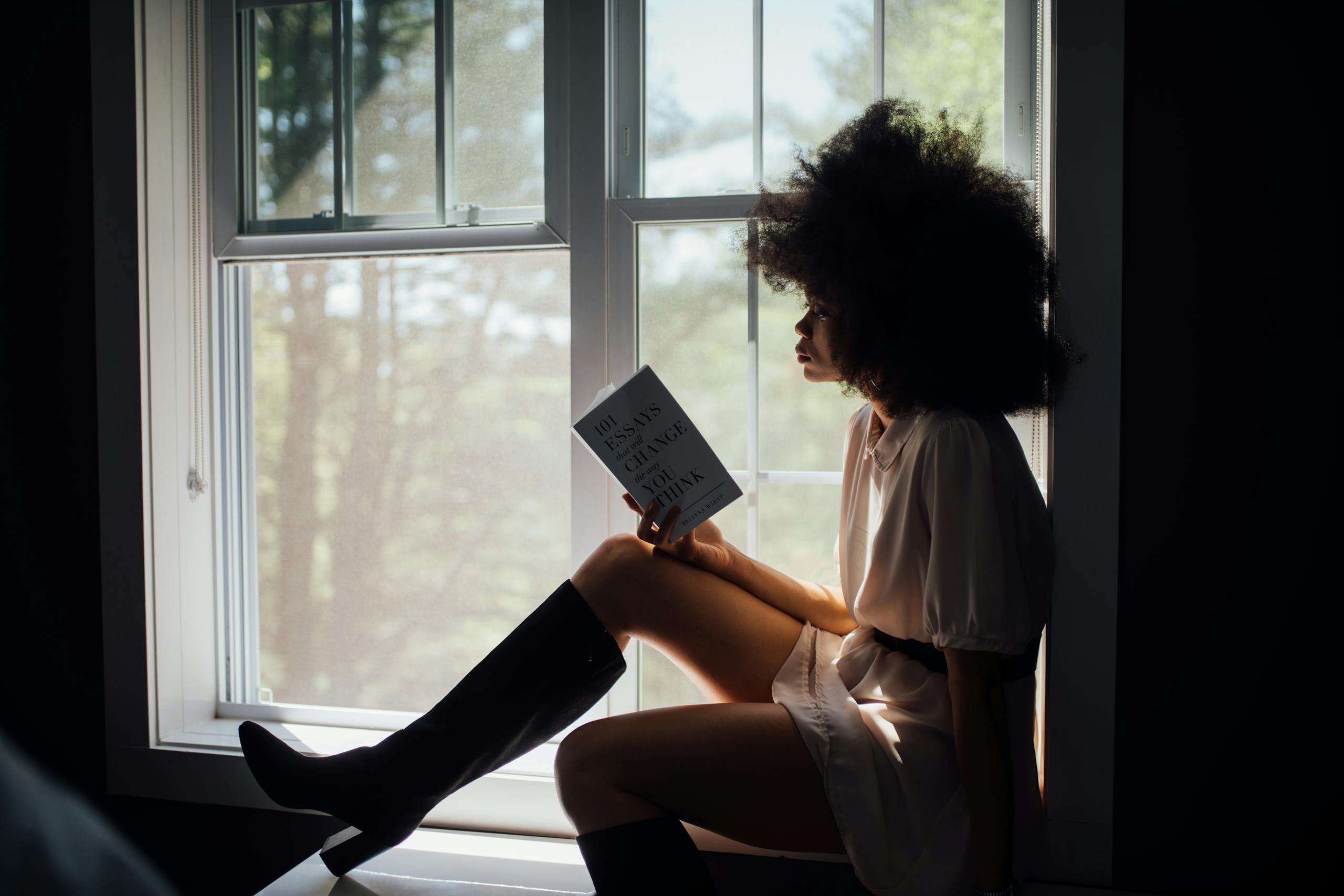 Woman reading peacefully by window with natural light streaming in.