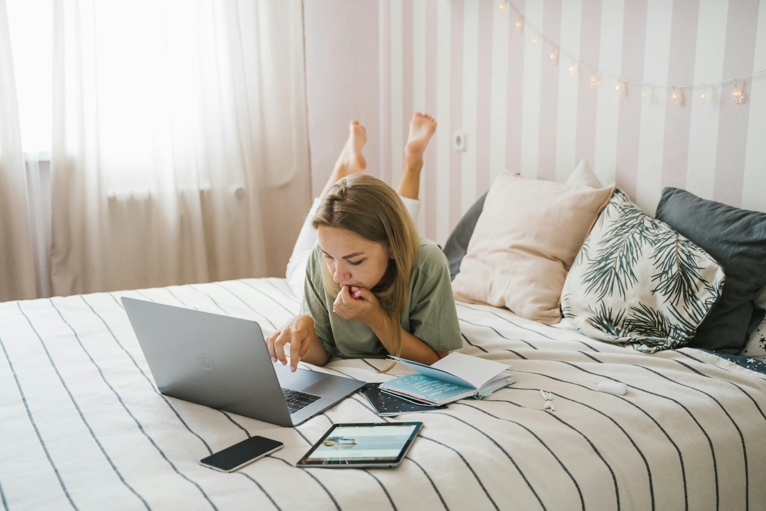 Woman lying on bed working remotely with laptop and tablet in bedroom